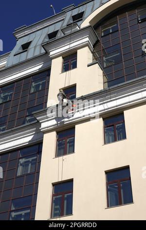 Industrial climber in protection outfit on the beige wall cleaning window glass Stock Photo