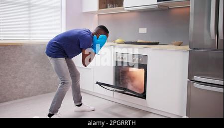 Shocked Young Man Looking At Smoke Coming Out Of Oven In Kitchen Stock Photo