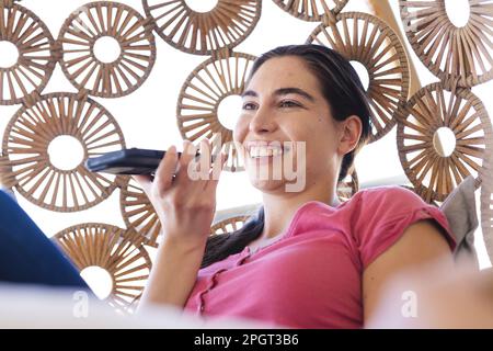 Happy caucasian young woman talking over mobile phone while sitting in swing at home. Unaltered, technology, lifestyle, speaker, communication and rel Stock Photo