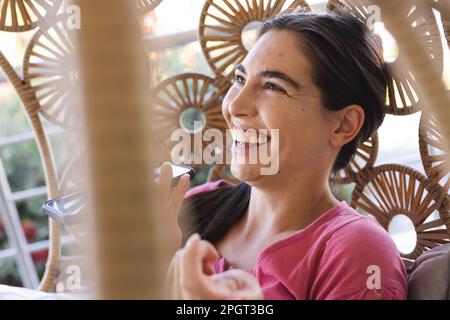 Close-up of cheerful caucasian young woman talking on speaker over smartphone while sitting in swing. Unaltered, technology, lifestyle, communication, Stock Photo