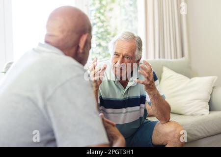 Two diverse senior male friends sitting in living room, talking during group therapy session. Senior lifestyle, friendship and support. Stock Photo