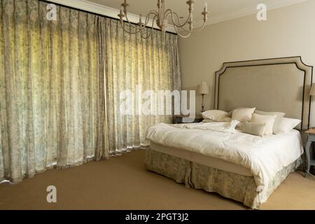 Chandelier hanging over cozy bed with cushions and pillows with beautiful curtains hanging on window. Copy space, unaltered, furniture, home and inter Stock Photo