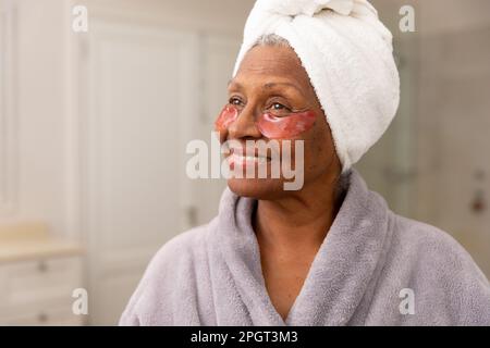 Closeup of smiling african american senior woman with eye patches under eyes looking away at home. Copy space, unaltered, body care, aging, portrait, Stock Photo