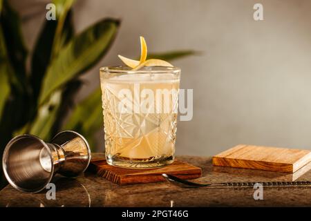 A glass of clear liquid with a metal measuring cup resting beside it on a wooden surface Stock Photo