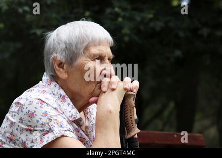 Portrait of elderly gray-haired woman sitting with walking sticks on a bench in a park. Healthy lifestyle in old age, life in retirement Stock Photo