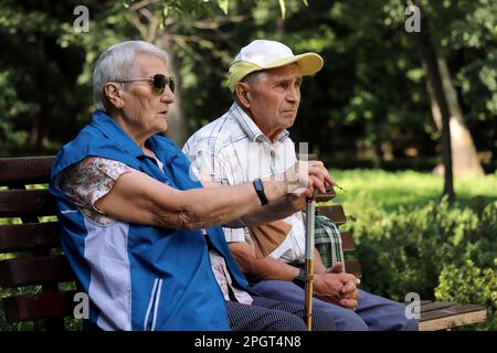 Elderly couple sitting on a bench in spring or summer park. Old man and woman outdoors, life in retirement Stock Photo