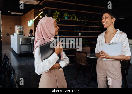 Happy two businesswomen talking to each other while working in cafe Stock Photo