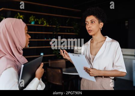 Happy two businesswomen talking to each other while working in cafe Stock Photo