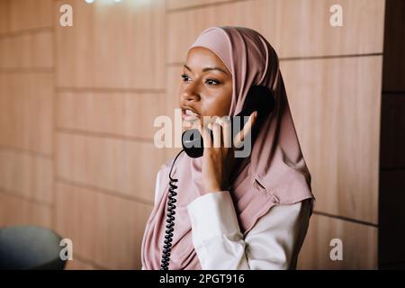 Muslim young businesswoman talking on phone while working at reception Stock Photo