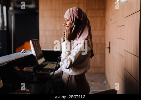 Muslim happy businesswoman talking on phone while working at reception Stock Photo