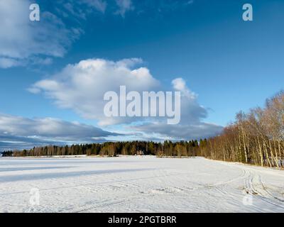 Vast snow-covered field under a bright blue sky with scattered clouds in northern Sweden Stock Photo