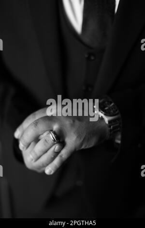 A vertical greyscale close-up of an man's hands as he places his wedding ring on his finger Stock Photo