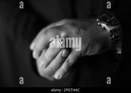 A greyscale close-up of an man's hands as he places his wedding ring on his finger Stock Photo