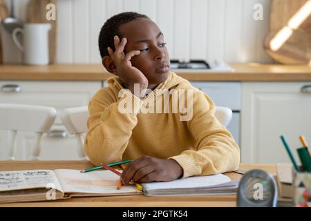 Thoughtful bored Black schoolboy look to side doing homework sits at table with textbooks at home Stock Photo