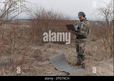 military man stands in camouflage and works with a laptop. Stock Photo