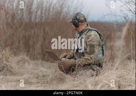 military man stands in camouflage and works with a laptop. Stock Photo