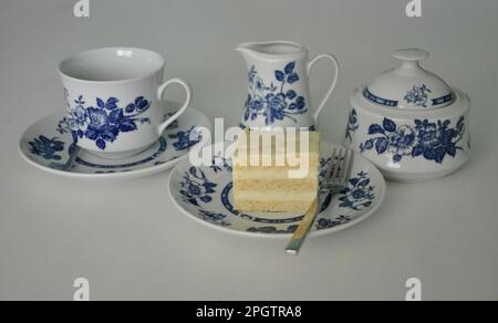 Coffee pot cup saucer cakes sugar spoon. Complete set of coffee service on a white background. Beautiful white dinner service with blue decoration . Stock Photo