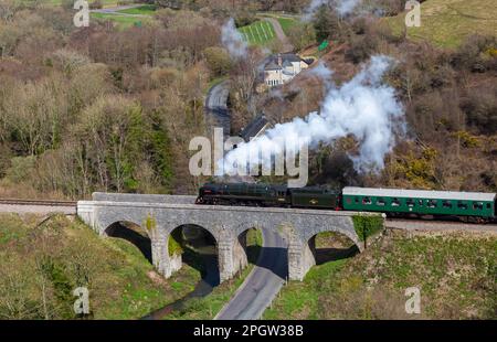 Corfe Castle, Dorset, UK. 24th March 2023. In February 1952, the British Railways Standard Class steam locomotive No. 70000 ‘Britannia’ had the sad honour of hauling the funeral train of King George VI, from King’s Lynn in Norfolk to London. Today the historic locomotive passes through Corfe Castle on a very windy day with sunny intervals, as part of the Swanage Railway’s Spring Steam Gala taking place from 24-26th March. Credit: Carolyn Jenkins/Alamy Live News Stock Photo