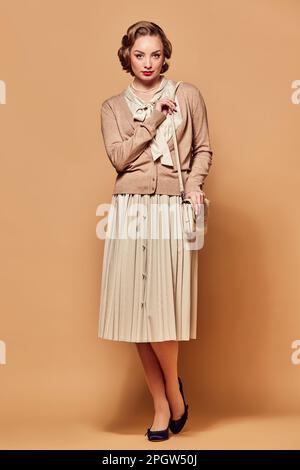 One pretty woman wearing vintage clothes standing with serious facial expression and looking at camera over beige background Stock Photo