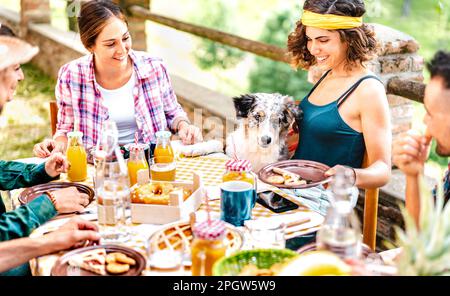 Young friends on healthy pic nic break fast with cute puppy at countryside farm house - Unplug life style concept with happy people having fun togethe Stock Photo