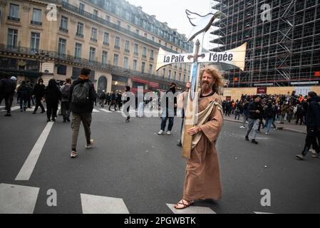 A man dressed as Jesus carries a cross with the message 'Peace, the sword' in the middle of a pitched battle during a general strike over the increase in the retirement age. The ninth strike day against the new pension reform of Macron's government was marked by many clashes between the police and the protesters. After Elisabeth Borne (Prime Minister of France) invoked Article 49.3 of the French Constitution to force the new law, thousands of people took the streets of Paris again at a demonstration that began at Place de la Bastille. Stock Photo