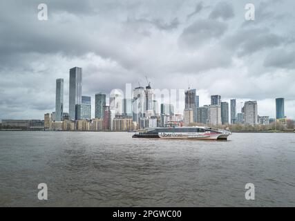 An Uber ferry boat passes the skyscraper buildings at Canary Wharf, one of London's financial districts, by the river Thames, England. Stock Photo