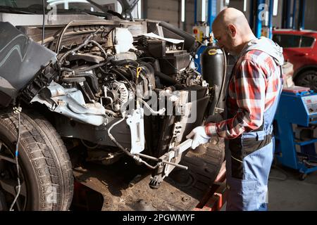 Middle-aged auto repairman stands in front of a disassembled car Stock Photo