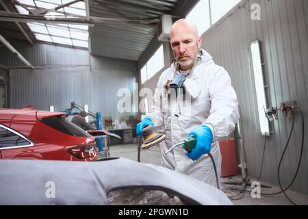Auto repair shop worker repairs part of car body Stock Photo