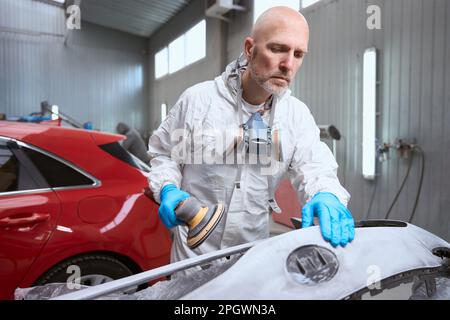 Man in overalls works with an unpainted car bumper Stock Photo
