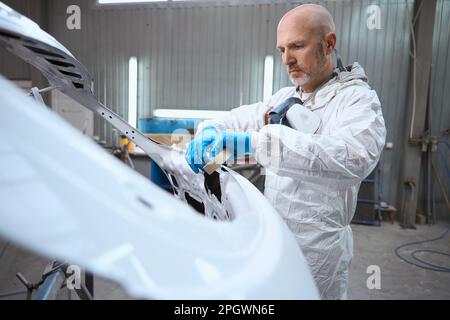 Employee of the paint shop prepares a part of the car body for work Stock Photo