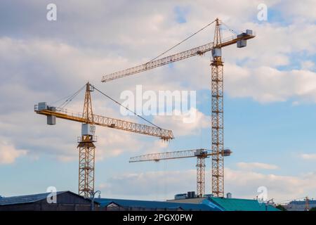Three yellow tower construction cranes against cloudy sky Stock Photo