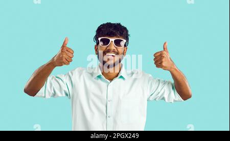 Portrait of happy cheerful young Indian man in sunglasses giving thumbs up and smiling Stock Photo
