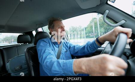 One older man driving in city in moving vehicle. Retired senior male caucasian person driver holding car steering wheel Stock Photo