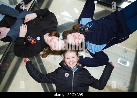 Tourist children child kid visitors to Tower Bridge pose to camera for photographst whilst lying on glass floors floor window in the high level walkways / walk way that joins the two towers. River Thames and car deck can be seen below. London, UK. (133) Stock Photo