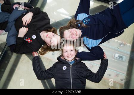 Tourist children child kid visitors to Tower Bridge pose to camera for photographst whilst lying on glass floors floor window in the high level walkways / walk way that joins the two towers. River Thames and car deck can be seen below. London, UK. (133) Stock Photo