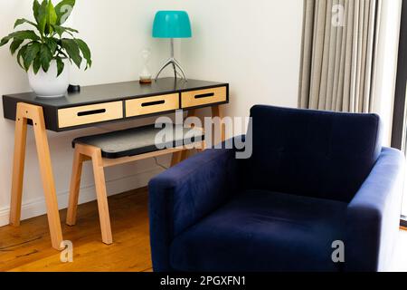 Corner of living room interior with armchair, plant and lamp on table with stool, and open curtains Stock Photo