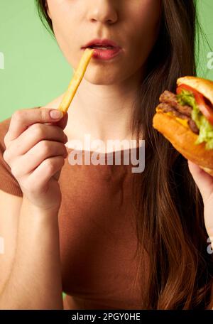 Portrait of woman holding hamburger cheeseburger while eating french fry Stock Photo