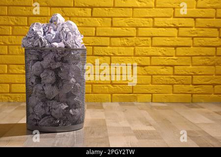 Trash bin full of paper on floor near yellow brick wall, space for text. Recycling rubbish Stock Photo