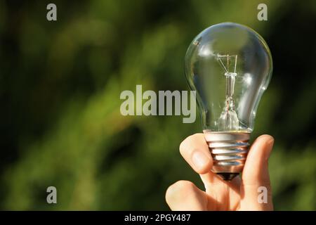 Woman holding incandescent light bulb on blurred green background, closeup. Space for text Stock Photo