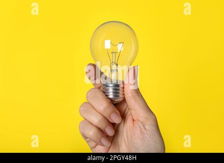 Woman holding incandescent light bulb on yellow background, closeup Stock Photo