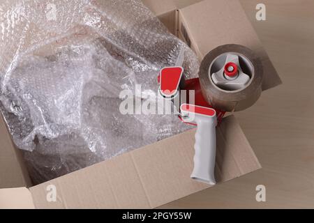 Cardboard box with bubble wrap and adhesive tape on wooden table Stock Photo