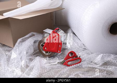 Adhesive tape with bubble wrap, scissors and cardboard box on table Stock Photo