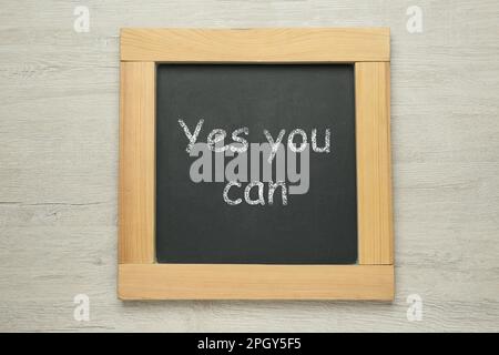 Small chalkboard with motivational quote Yes you can on white wooden background, top view Stock Photo