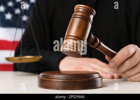 Judge with gavel at white wooden table near flag of United States, closeup Stock Photo