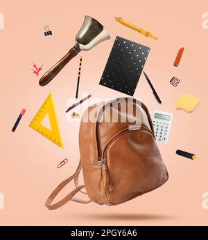 Leather backpack, school bell and different stationery flying on beige background Stock Photo