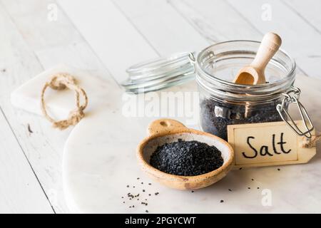 A jar and bowl filled with black Hawaiian rock salt on a marble slab. Stock Photo