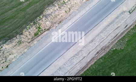 Asphalt road under construction between two green fields. View from the drone Stock Photo