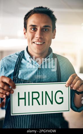 Staff wanted. a young man holding up a hiring sign in his store. Stock Photo
