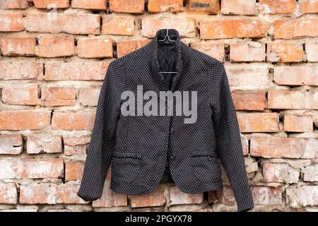 black womens blazer with polka dots hanging on a brick old wall outside in the sun Stock Photo