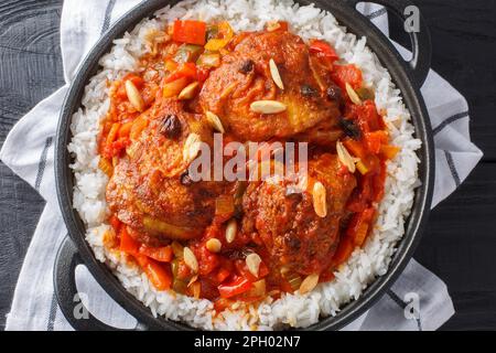 Country Captain chicken fried and then stewed with vegetables, raisins, almonds, tomato sauce and curry, served with rice in a pan on the table. Horiz Stock Photo